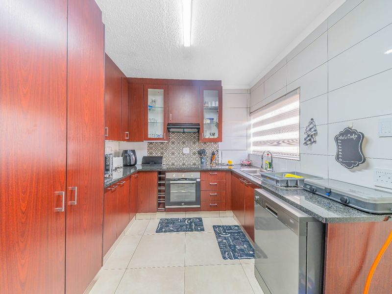 A functional kitchen featuring dark wood cabinetry, granite countertops, built-in oven, extractor fan, and tiled splashbacks with neutral floor tiles.