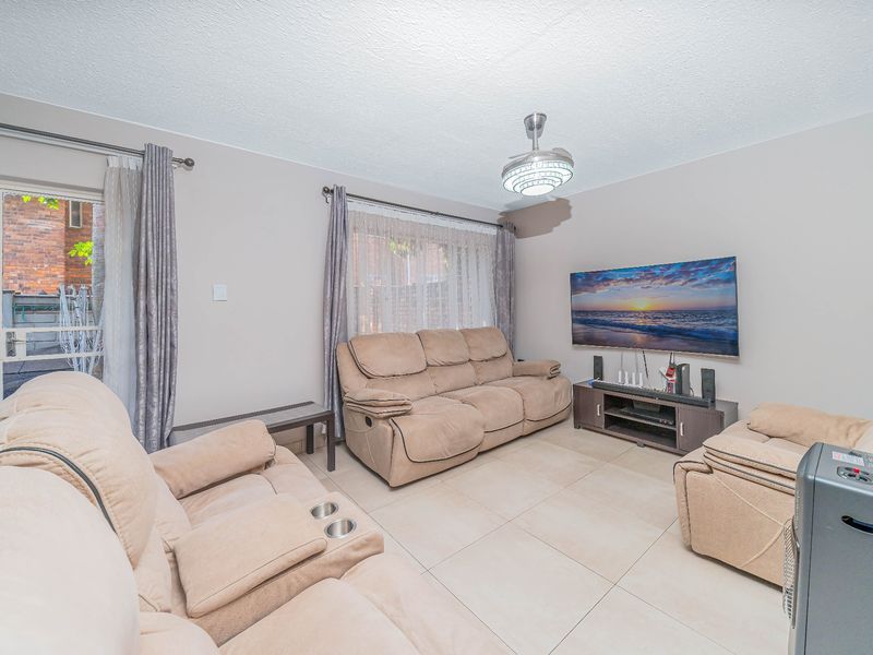 A well-maintained living room featuring neutral tiled flooring, a modern ceiling fan, and direct access to an outdoor area through a sliding glass door.