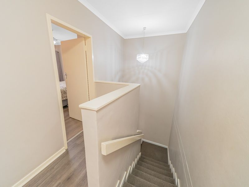 A clean and well-maintained hallway landing featuring a staircase with a handrail, neutral wall finishes, and a mix of laminate and carpeted flooring.