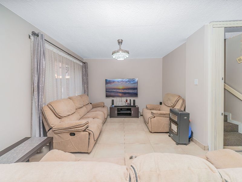 A comfortable living room featuring tiled flooring, a ceiling fan, and direct access to the staircase.