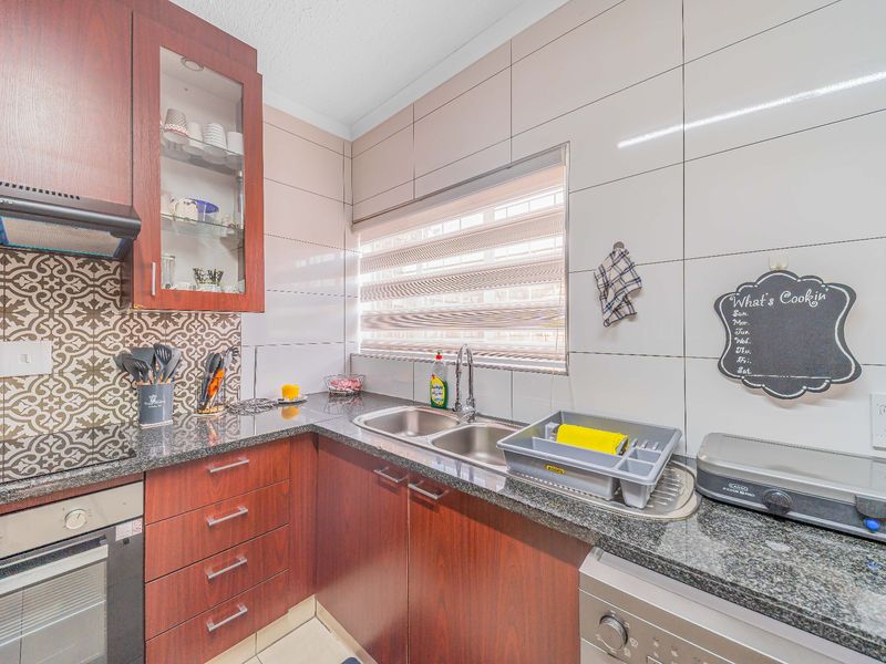A functional kitchen featuring dark wood cabinetry, granite countertops, a double bowl sink, and integrated appliances including an oven and hob.