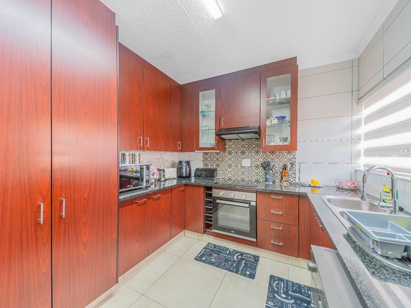 A functional kitchen featuring dark wood cabinetry, granite countertops, a built-in oven, extractor fan, and a double basin sink with a patterned tile backsplash.