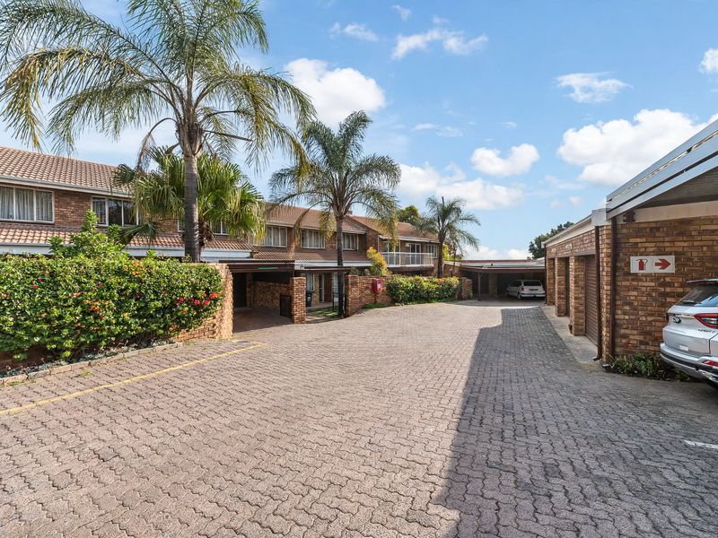 Front view of a townhouse complex featuring a paved driveway, brick facade, and multiple garage units with established landscaping.