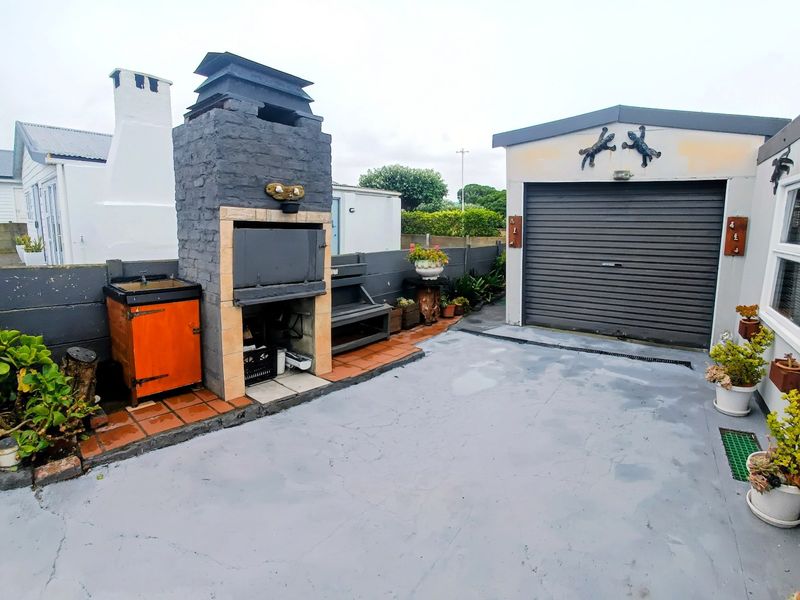 Rear courtyard area featuring a built-in braai, concrete paving, and access to a single garage with a roller shutter door.