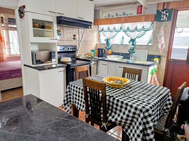 A functional kitchen featuring built-in cabinetry, laminate countertops, a freestanding stove with extractor fan, and tiled backsplash, offering potential for modern updates.