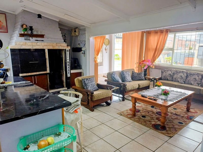 Open-plan living area featuring a built-in indoor braai, stone fireplace surround, tiled flooring, and large windows providing natural light.