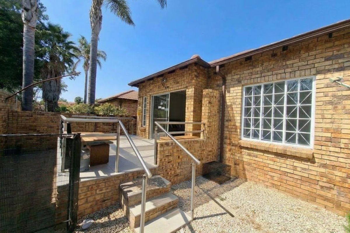 Rear view of the townhouse featuring a face brick facade, a raised tiled patio with stainless steel balustrades, and a low-maintenance gravel garden area.