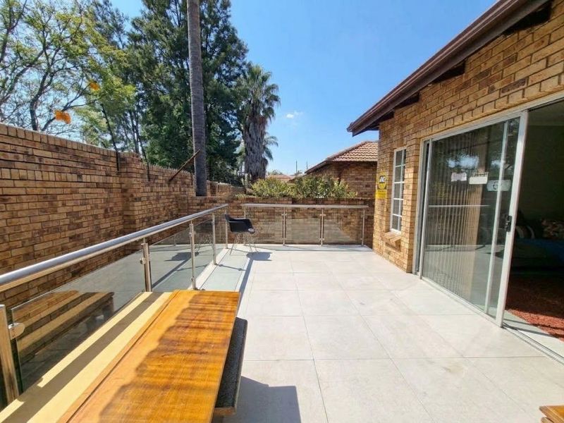 A spacious outdoor patio featuring modern glass and stainless steel balustrades, tiled flooring, and direct access to the interior through a large sliding door.