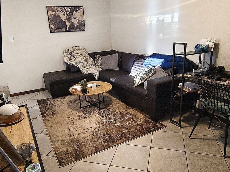 A functional living room area featuring tiled flooring, providing a versatile space for relaxation and home office setup.
