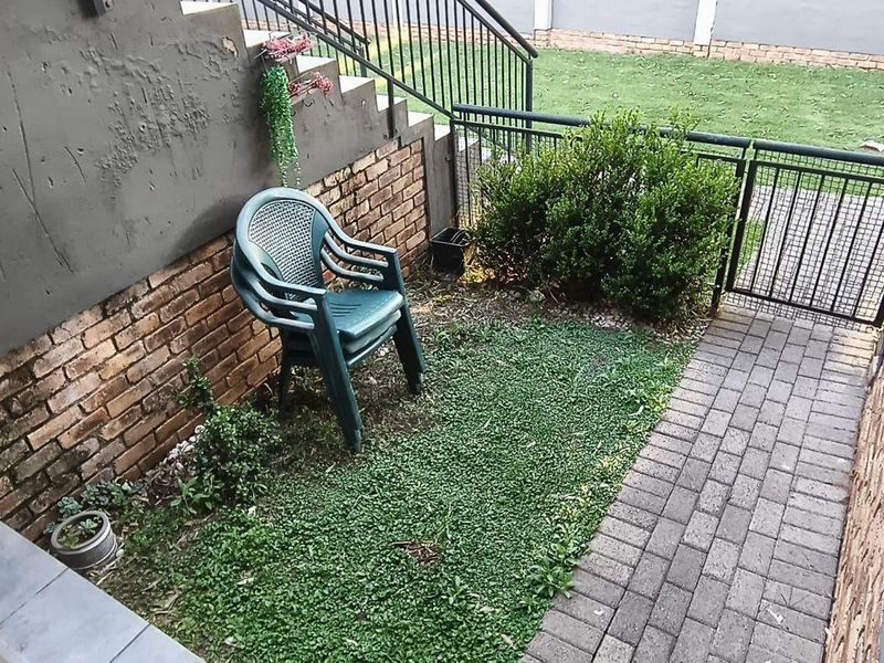 A small rear courtyard area featuring a brick retaining wall, paved walkway, and metal security gate, requiring maintenance to address wall damage and landscaping.