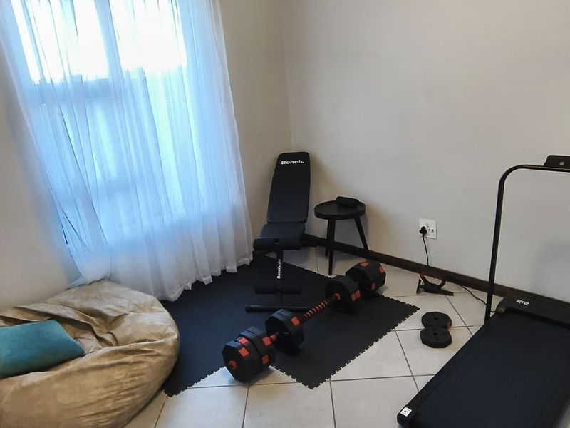 A small, functional room currently utilized as a home gym, featuring tiled flooring and natural light from a window.