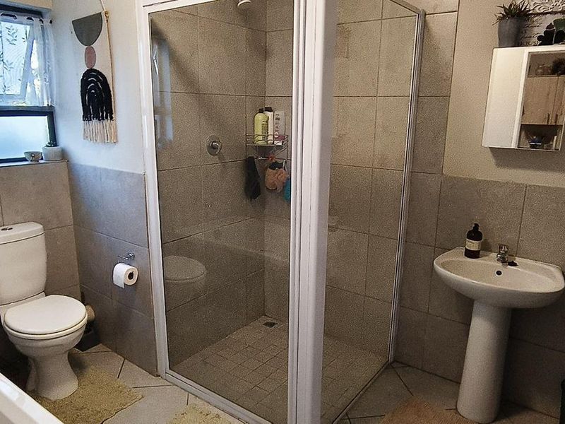 A functional bathroom featuring a glass-enclosed shower, pedestal basin, and toilet with neutral wall and floor tiling.