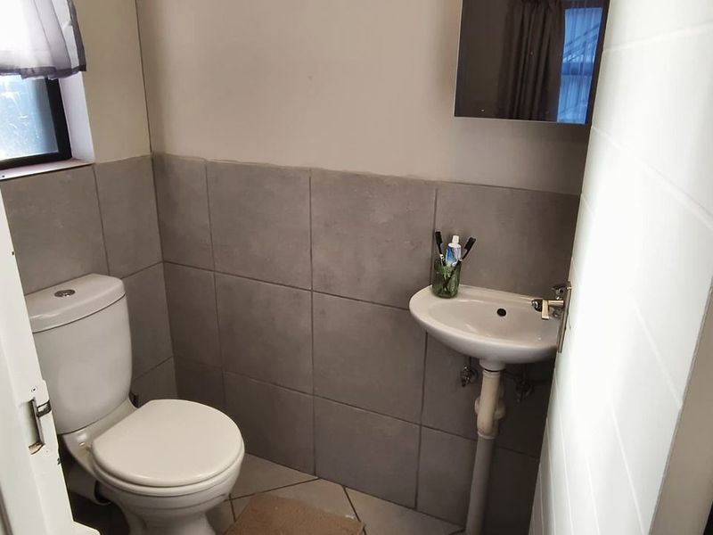 A compact guest bathroom featuring a white toilet, pedestal basin, and neutral grey wall tiling.