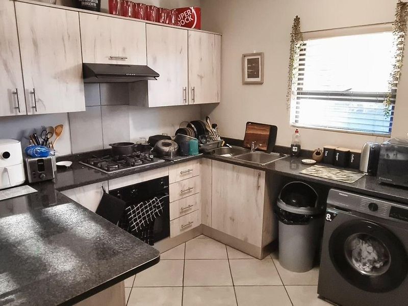 Functional kitchen featuring light wood-look cabinetry, granite countertops, gas hob, built-in oven, and integrated laundry plumbing with tiled flooring.