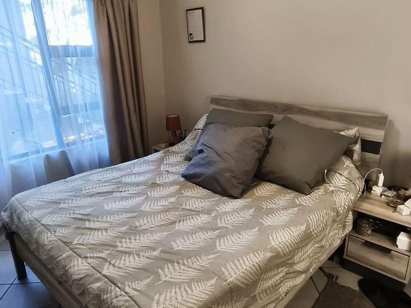 A functional bedroom featuring tiled flooring and large windows with curtain treatments, providing a comfortable and well-lit living space.
