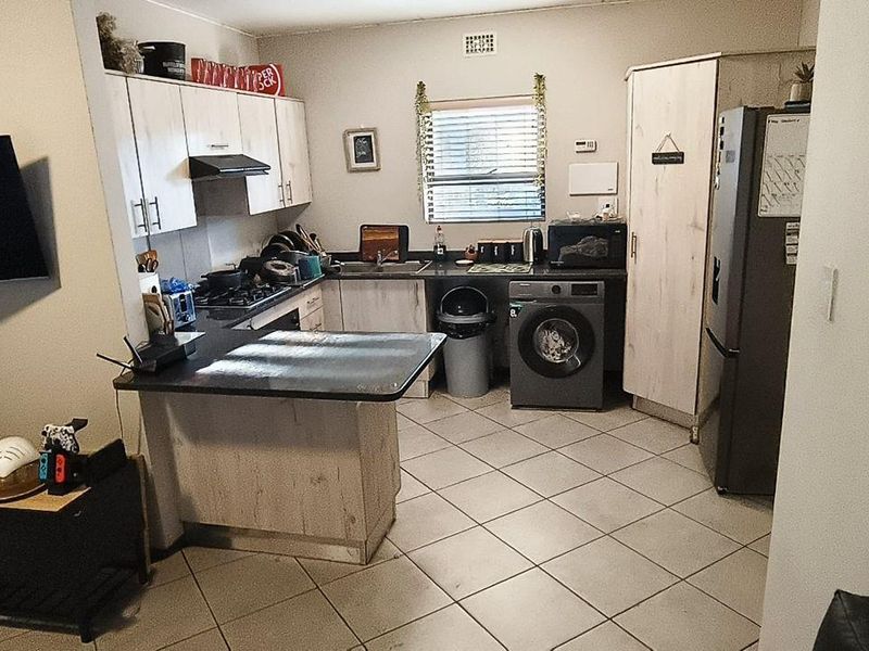 Open plan kitchen and living area featuring tiled flooring, built-in cabinetry with laminate countertops, and integrated gas hob with extractor fan.