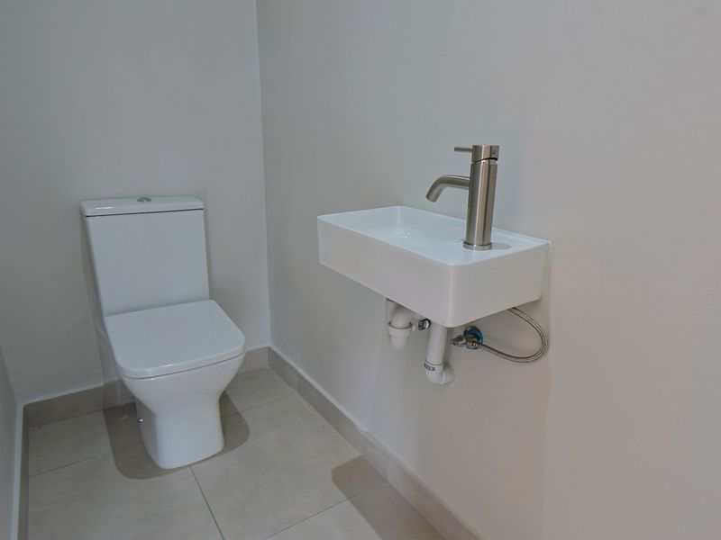 A clean and modern guest cloakroom featuring a wall-mounted basin with a contemporary mixer tap and a white close-coupled toilet.