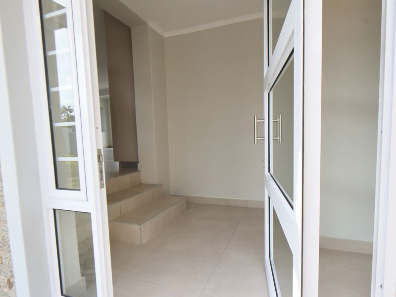A bright and modern entrance foyer featuring tiled flooring, glass panelled doors, and internal steps leading to the main living area.