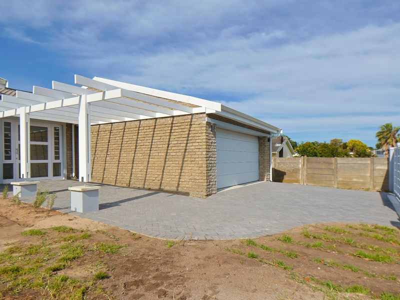 Front exterior view featuring a paved driveway, brick facade, white pergola structure, and a secure garage with a sliding gate entrance.