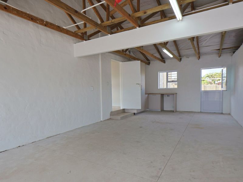 Spacious garage area featuring exposed timber roof trusses, concrete flooring, and a small built-in kitchenette area with a stable door leading outside.