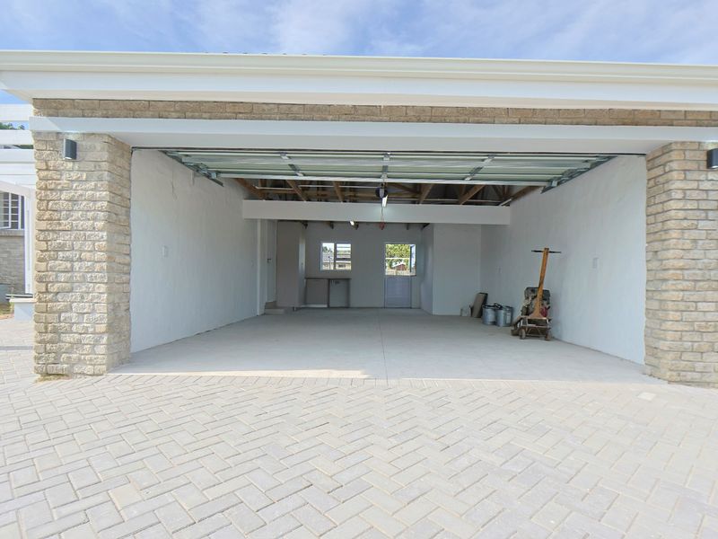 A spacious, open-plan double garage featuring a brick facade, concrete driveway, and exposed roof trusses, providing ample storage or parking space.