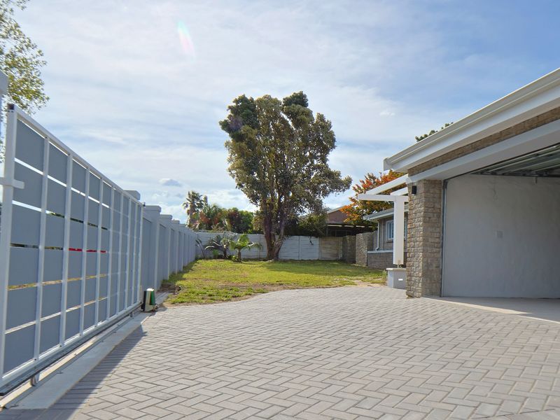 Front view of the property featuring a paved driveway, sliding gate, boundary wall, and access to the garage.