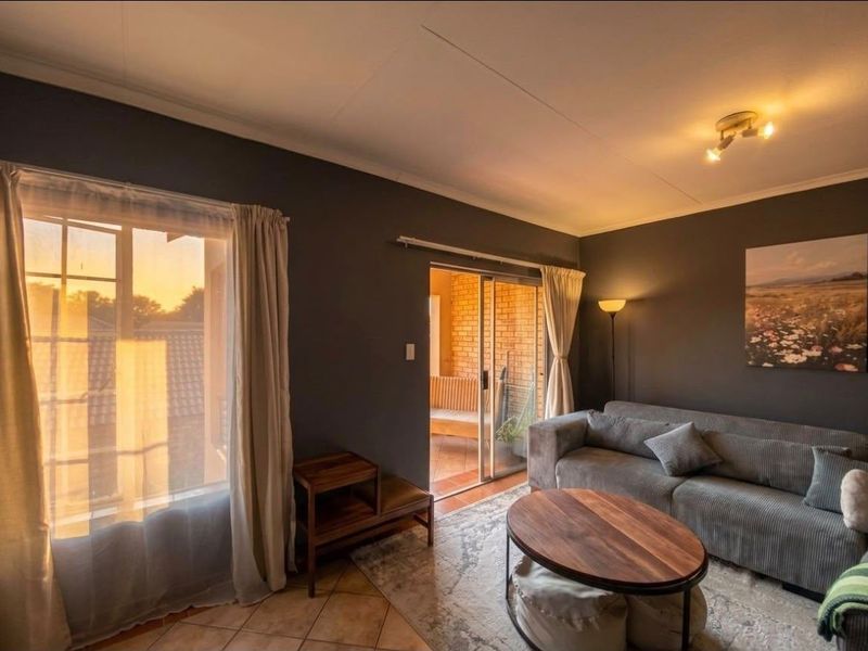 A cozy living room featuring tiled flooring, a sliding glass door leading to a balcony, and warm ambient lighting.