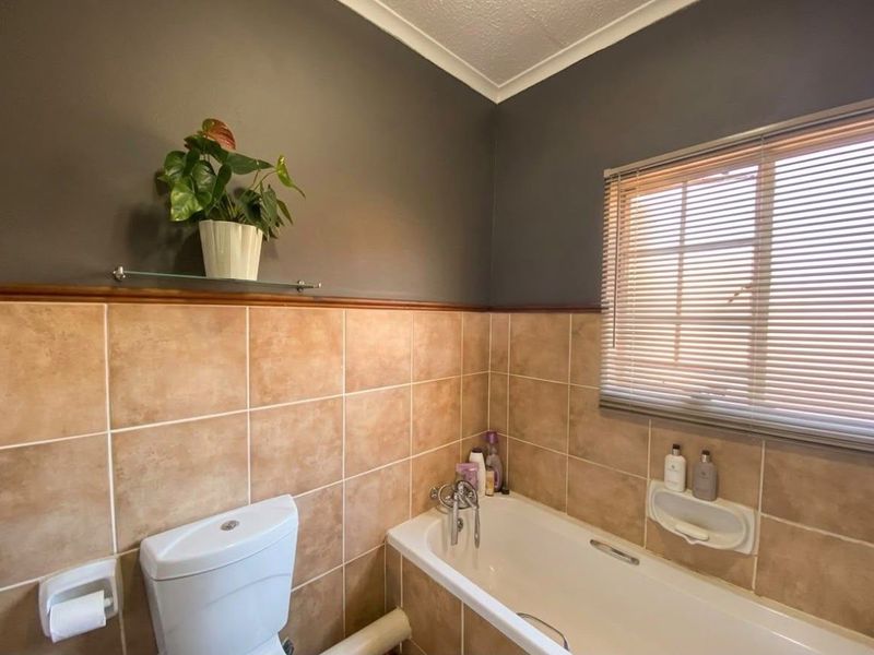A functional bathroom featuring a bathtub, toilet, and tiled wall finishes with a window providing natural light.