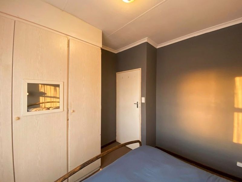 A bedroom featuring built-in cupboards, dark grey accent walls, and cove cornicing, offering a functional space with potential for modern updates.