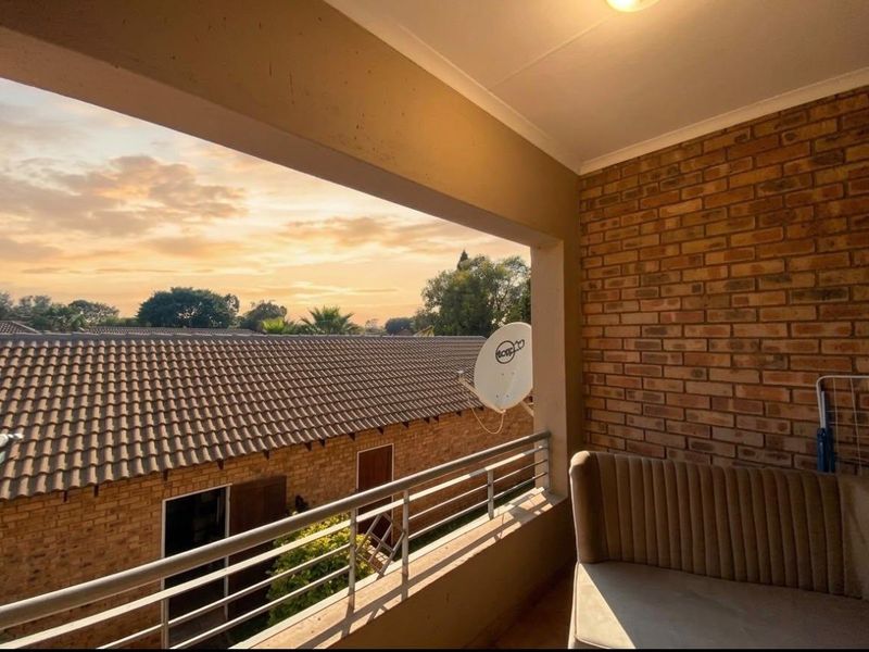 A covered balcony featuring an exposed brick wall and metal railing, offering an elevated view of the surrounding residential complex.