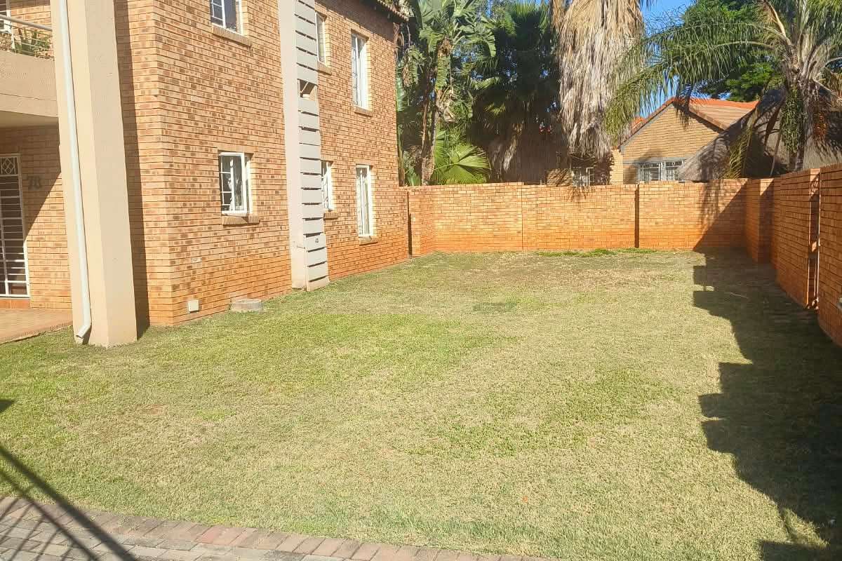 A private rear garden area featuring a well-maintained lawn, paved walkway, and secure perimeter brick walling adjacent to the apartment building.