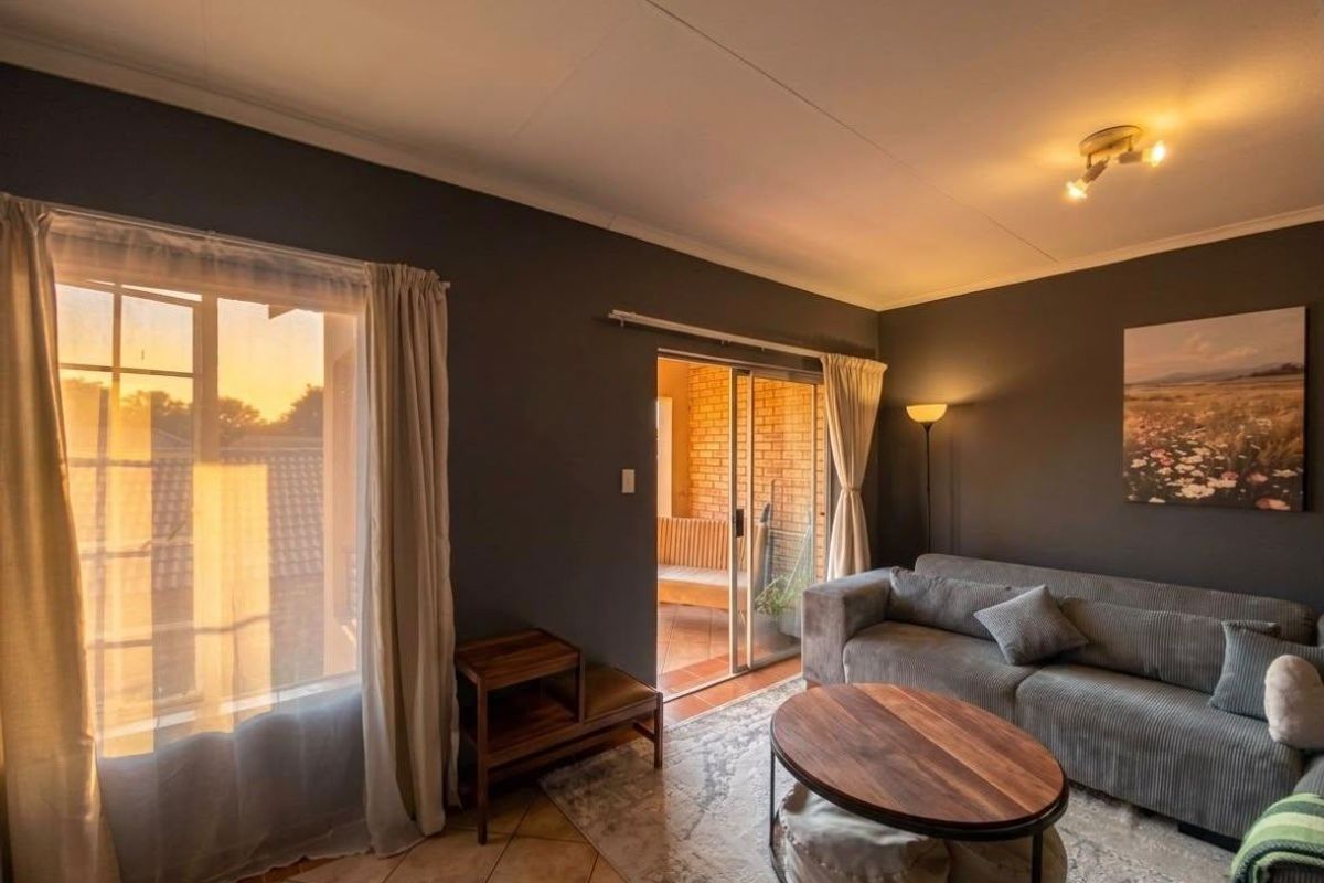 A cozy living room featuring tiled flooring, a sliding glass door leading to a balcony, and warm ambient lighting.