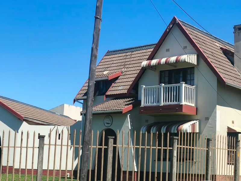 Front elevation of a two-story house featuring a tiled roof, balcony, and attached garage, enclosed by perimeter fencing.