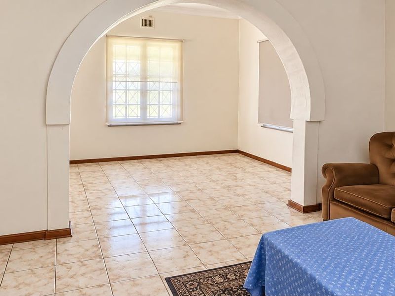 A living area featuring a distinctive arched doorway, tiled flooring, and natural light through a window with security bars.