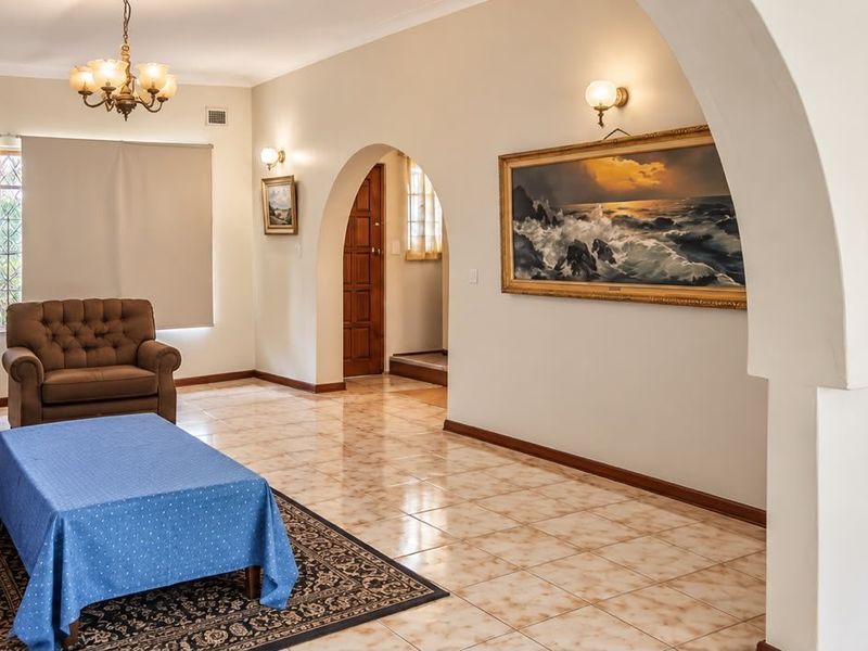 Spacious living area featuring ceramic tile flooring, distinctive arched architectural details, and warm wall sconce lighting, creating a classic and inviting atmosphere.