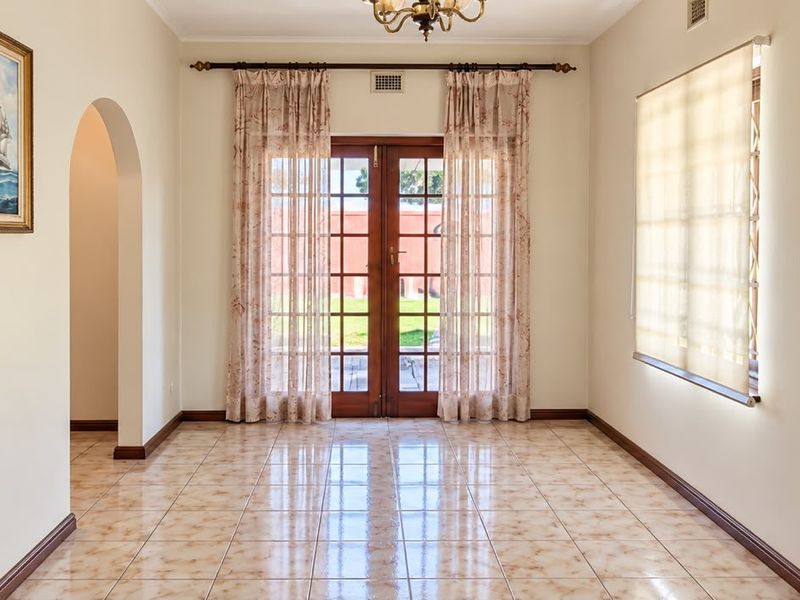 A bright and spacious living area featuring ceramic tile flooring, an elegant arched doorway, and classic french doors leading to the exterior.