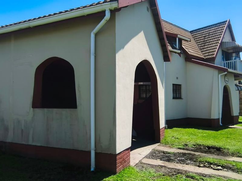 Rear view of the property featuring a plastered facade with arched architectural details, tiled roofing, and surrounding lawn area.