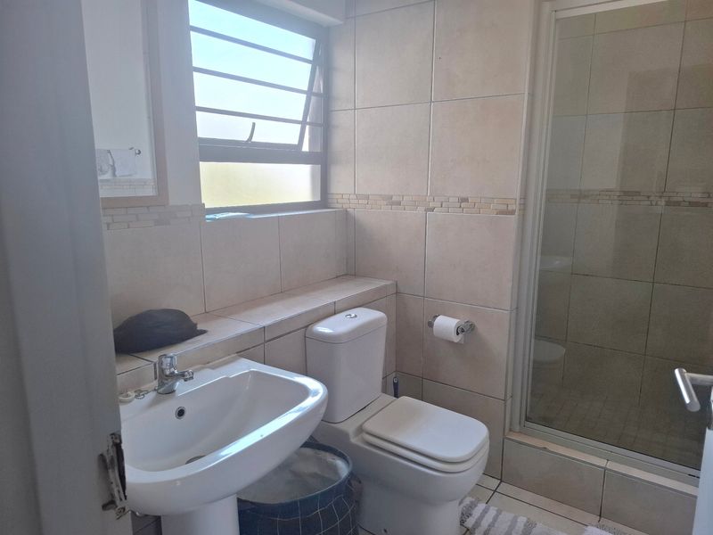 A functional bathroom featuring a pedestal basin, toilet, and a glass-enclosed shower with neutral wall and floor tiling.