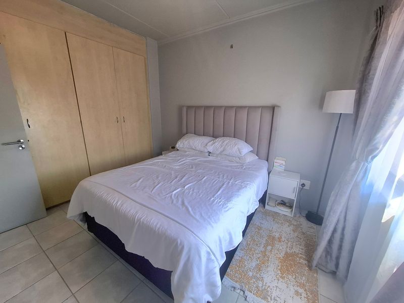 A functional bedroom featuring built-in wooden cupboards and tiled flooring, offering a neutral space ready for personalization.