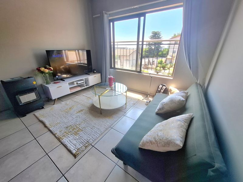A bright living room featuring tiled flooring and a large sliding glass door that provides natural light and access to the balcony.