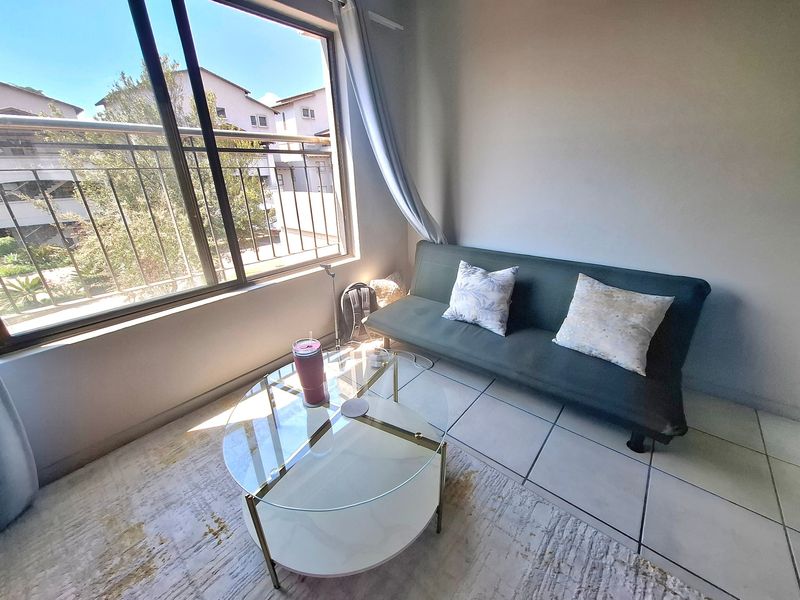 A bright living area featuring large sliding glass doors that open onto a balcony, with neutral tiled flooring throughout.