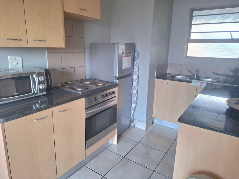 Functional kitchen featuring light wood cabinetry, granite countertops, built-in oven with electric hob, and a stainless steel double sink with tiled flooring.