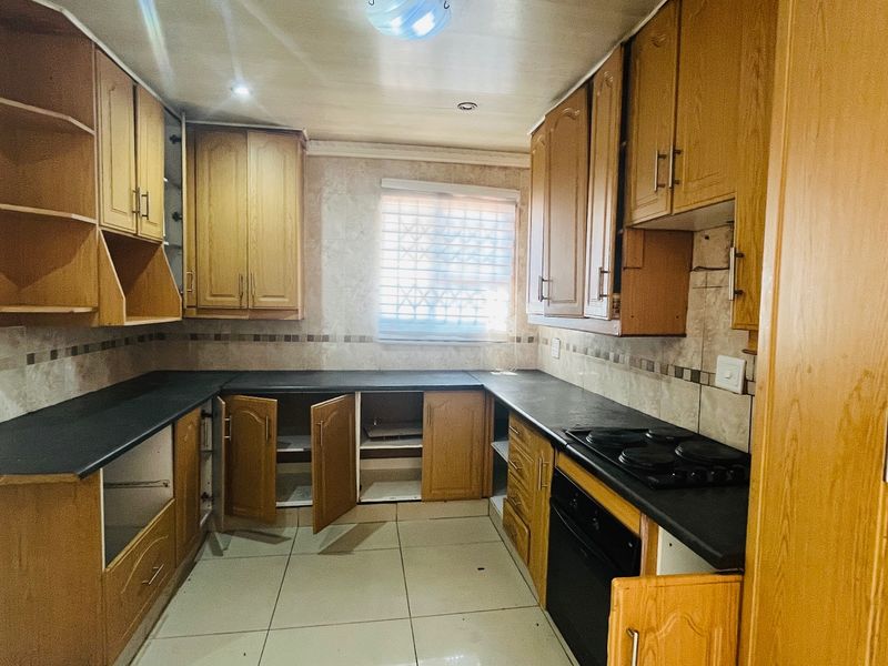 A dated kitchen featuring wooden cabinetry, black countertops, and integrated appliances. The space is vacant and requires cosmetic updates to modernize the finishes.