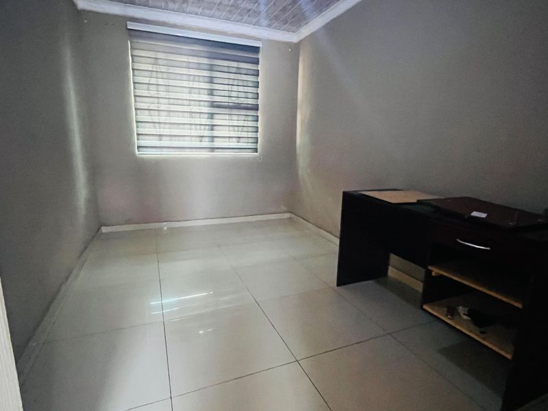 A simple, empty bedroom featuring tiled flooring, a window with roller blinds and security bars, and a coved ceiling.