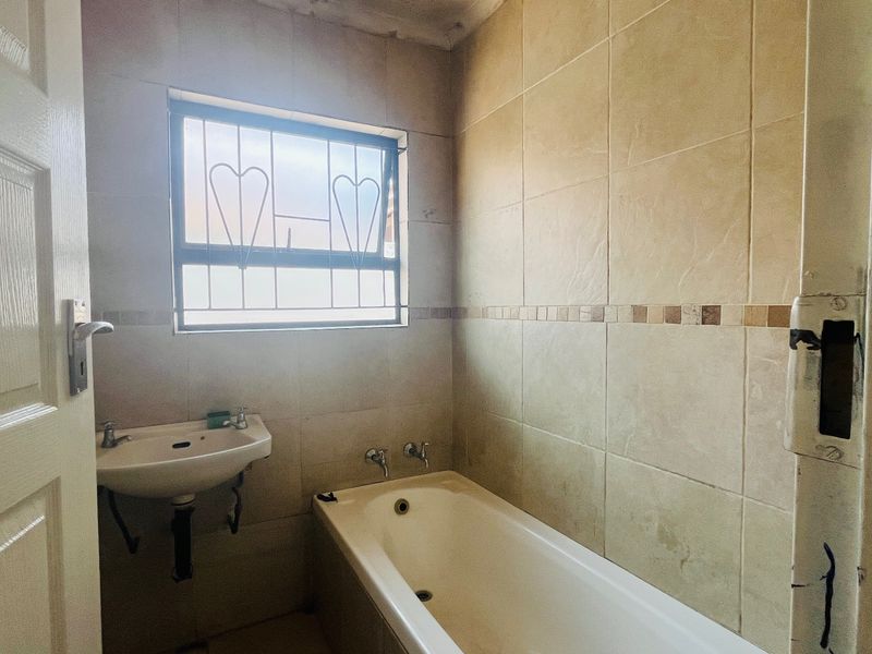 A compact bathroom featuring a bathtub, wall-mounted basin, and neutral wall tiling, requiring some cosmetic updates to the door frame and fixtures.