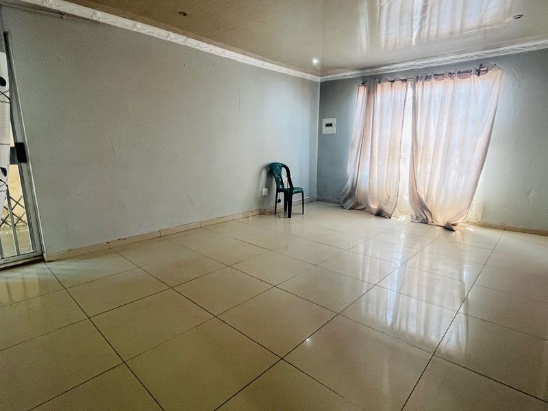 A spacious, empty living room featuring neutral tiled flooring, recessed ceiling lighting, and a sliding glass door providing access to the exterior.
