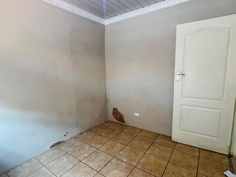 An empty bedroom featuring tiled flooring and a panel door, currently requiring wall repairs and repainting to restore its condition.