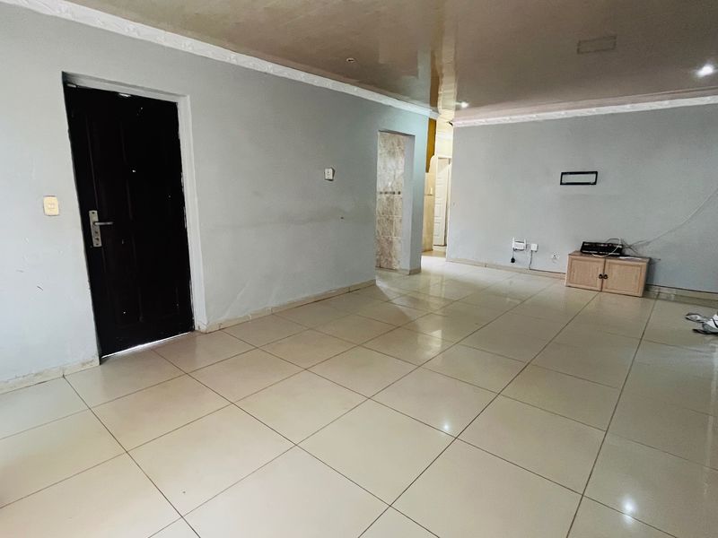 A spacious, empty living area featuring neutral tiled flooring, a glossy ceiling with decorative cornice, and a dark internal door.