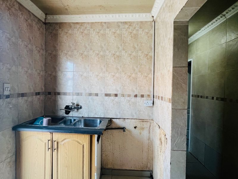 A small scullery or utility area featuring a stainless steel sink, tiled splashback, and built-in cabinetry, requiring cosmetic repairs and refurbishment.