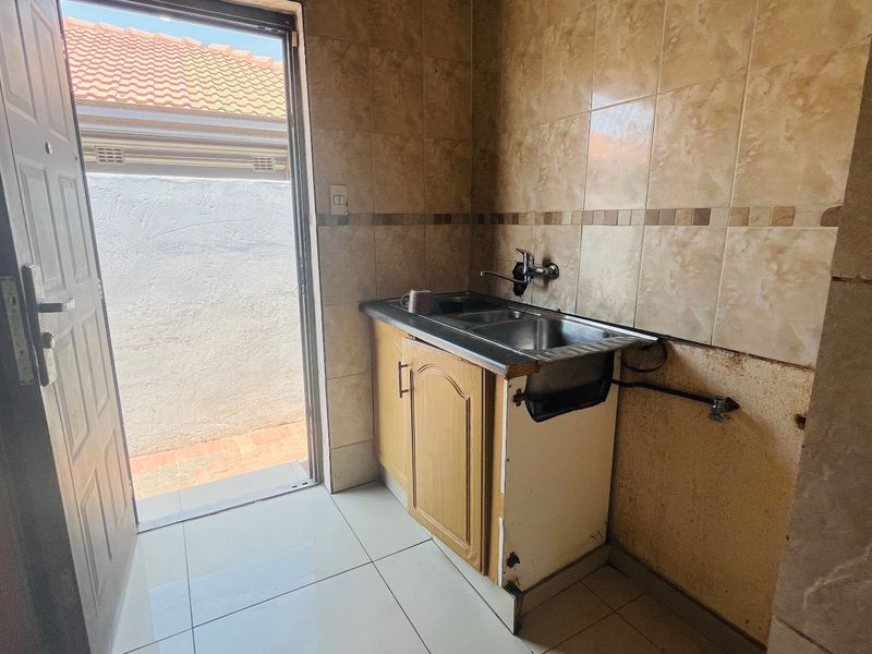 A functional laundry area featuring a stainless steel sink, tiled splashback, and tiled flooring, with direct access to an outdoor space.